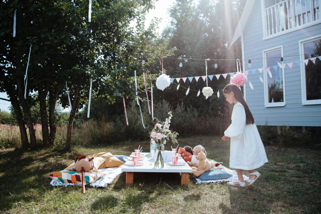 A child's tea party setup under trees with decorations and sunlight in a garden setting.