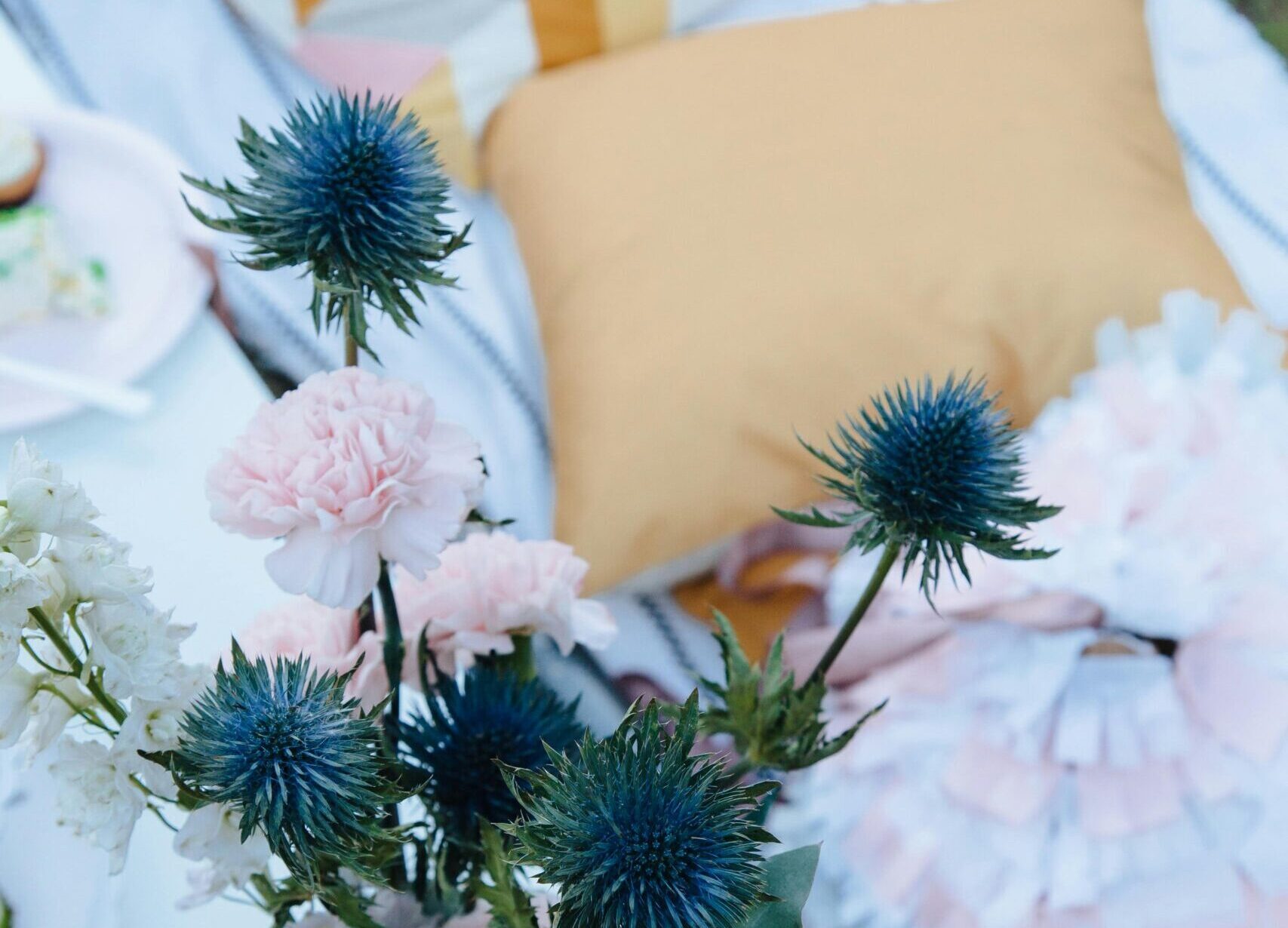 Stylish picnic setup with colorful pillows and vibrant floral bouquet outdoors.
