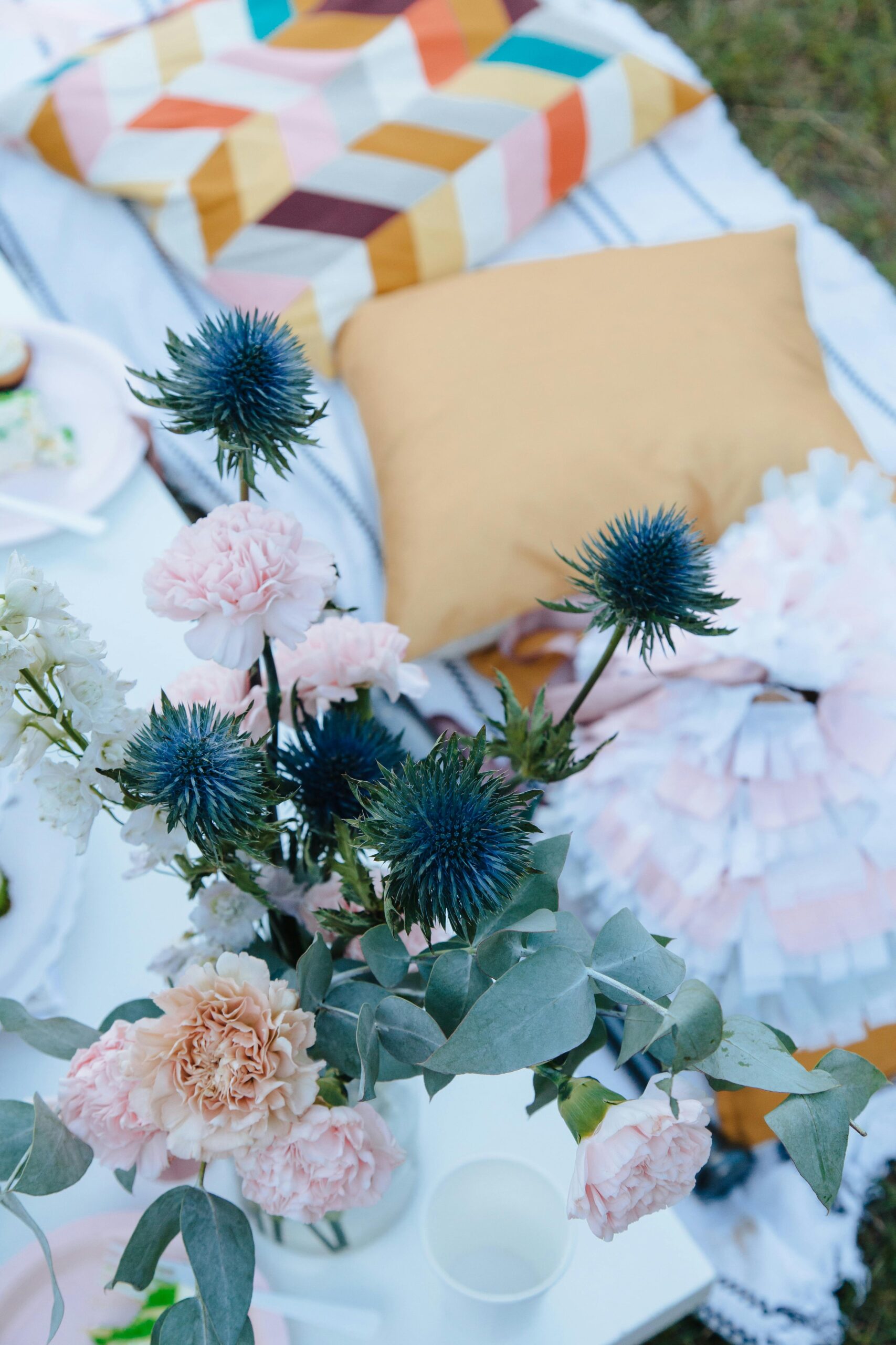 Stylish picnic setup with colorful pillows and vibrant floral bouquet outdoors.